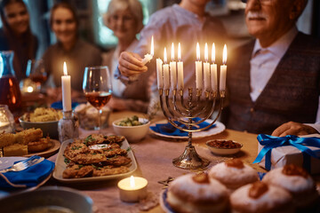 Close up of kid lighting the menorah during family dinner on Hanukkah.