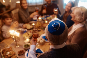 Rear view of senior Jewish man toasting with his family during meal at dining table on Hanukkah.