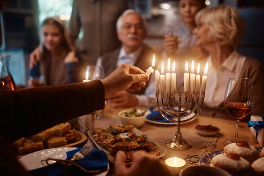 Close up of Jewish man lighting menorah during family dinner on Hanukkah.