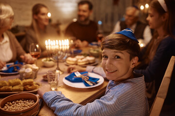 Happy Jewish boy having family dinner at dining table on Hanukkah and looking at camera.