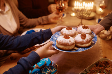 Close up of Jewish family having Hanukkah jam filled donuts for dessert at dining table.