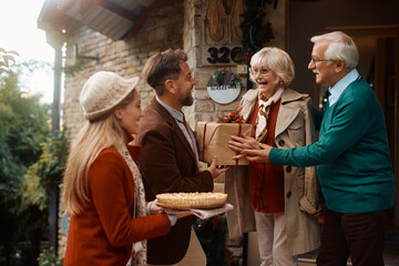 Happy senior couple welcoming their son and his wife at doorstep on Thanksgiving.
