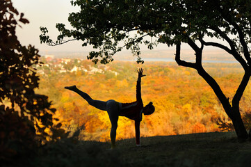 Silhouette of a woman practicing yoga against autumn background