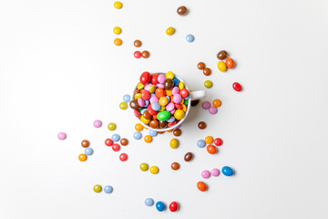 Taza blanco con bolas de chocolate de colores con fondo blanco y mano cogiendo golosinas