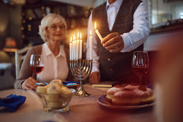Close up of senior man celebrating Hanukkah with his wife and lighting menorah at home.