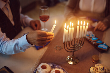 Close up of senior Jewish man lighting menorah at home.