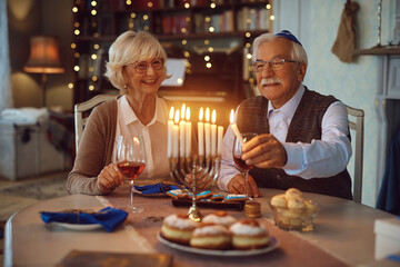 Happy senior couple lighting candles in menorah while celebrating Hanukkah at home.
