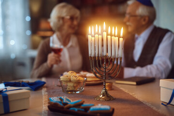 Lit candles in menorah with mature Jewish couple in background.