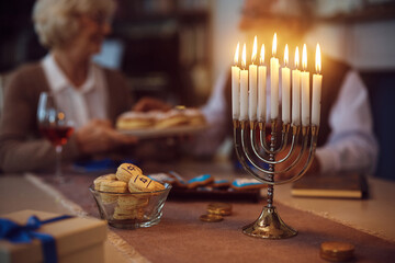 Traditional Hanukkah candles in menorah with senior couple in background.