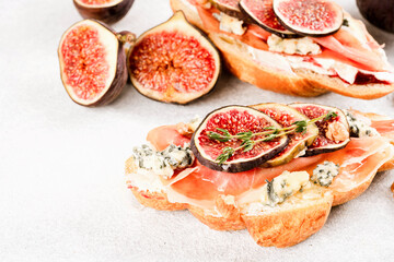 Fresh croissant bruschetta with ripe fig, blue cheese, prosciutto, walnuts and herbs over white concrete table background. Selective focus