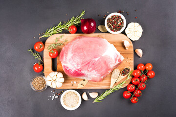 Top view on boneless raw pork shoulder ready for roasting with seasonings and vegetables over dark concrete background. Organic meat for main dish. View above