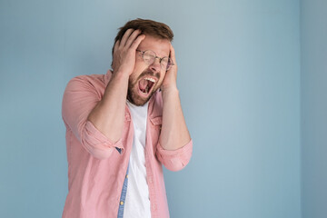 Attractive man in stress and despair, he screams loudly widely and holds head with hands. Copy...