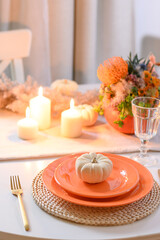 Thanksgiving day table setting with fall decorations, centerpiece of colorful flowers in pumpkin as vase on white table. Close up. Vertical format.