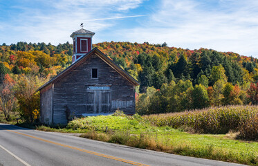 Fototapeta na wymiar Small wooden barn with red cupola set against vibrant Vermont fall colors