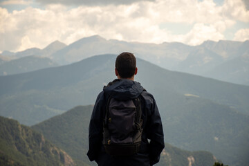 Young backpacker wearing a dark raincoat and enjoying the mountain views.