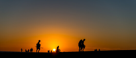 Panoramic view of silhouettes of a group of people walking along the coastline at a beautiful sunset