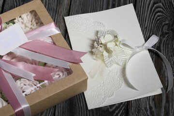 Fototapeta na wymiar Homemade marshmallows in a gift box. Tied with ribbon. Zephyr flowers. Homemade greeting card in white. With decorative elements. Ribbons, flowers and leaves are attached to cardboard.