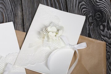 Homemade greeting card in white. With decorative elements. Ribbons, flowers and leaves are attached to cardboard. Paper envelope. Close-up.