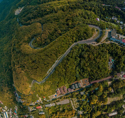 above the serpentine highway in the mountains of the Caucasus covered with green forest - aerial view