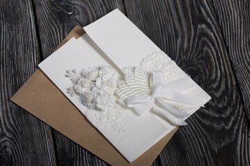 Homemade greeting card in white. With decorative elements. Ribbons, flowers and leaves are attached to cardboard. Paper envelope. Close-up.