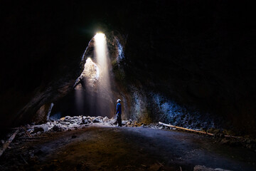 Adventurous athletic male standing in a lava tube looking at the sunlight shinning down into the cave through holes in the ceiling.