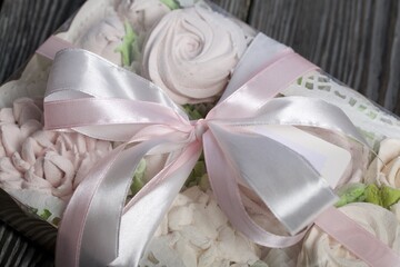 Homemade marshmallows in a gift box. Tied with ribbon. Zephyr flowers. On black pine boards. Taken from above.