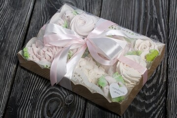 Homemade marshmallows in a gift box. Tied with ribbon. Zephyr flowers. On black pine boards. Taken from above.