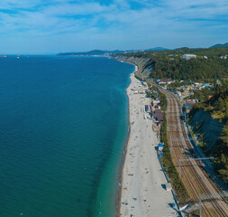 rocky steep coast of the Black Sea with pebble beaches and a railway at the foot of the Caucasus Mountains - aerial  view on a sunny day