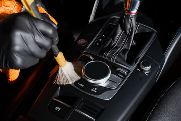 Dry cleaning with brush of gearbox and dashboard in car. Auto detailing service. Cleaning individual elements of black leather interior in auto. - obrazy, fototapety, plakaty