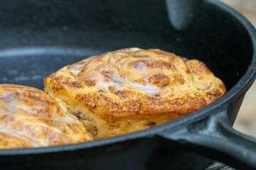 cinnamon buns cooked in cast iron pan outside on a fire. Camping cooking concept shot.