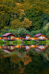 Fototapeta na wymiar Wooden houses on the water near the forest for carp fishing. A place to relax in nature. Autumn carp fishing season.