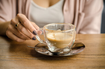 Young woman with blond hair and a white shirt is holding a cup of latte or cappuccino in a cafe. Lunch is over