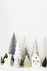 Merry Christmas! Stylish little Christmas trees and house decorations on white table. Modern christmas scene, miniature snowy village. Winter holiday banner, scandinavian monochromatic decor