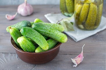 A clay bowl with fresh cucumbers and glass jars with pickles.