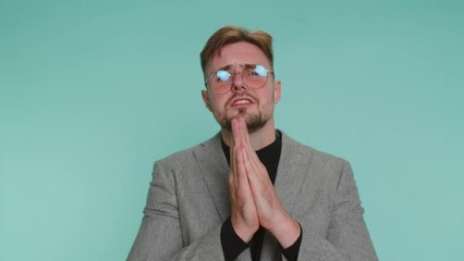 Please, God help. Sad worried business man praying, looking upward, making wish asking with hopeful imploring expression begging apology, forgiveness. Young adult guy isolated alone on blue background