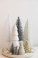 Stylish little Christmas trees on plate on white table. Festive Christmas scene, miniature snowy forest, table setting. Modern minimal scandi decorations. Merry Christmas and Happy Holidays