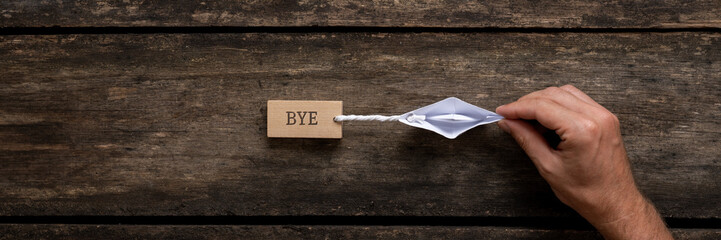 Wide view image of male hand holding an origami made paper boat pulling a wooden peg with Bye sign...