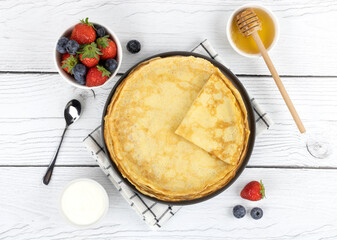 French pancakes, pancakes with berries, honey, sour cream on a white wooden background. Pancakes...