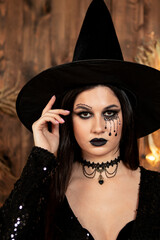young girl in the image of a witch, wearing a black hat and a black dress with a make-up