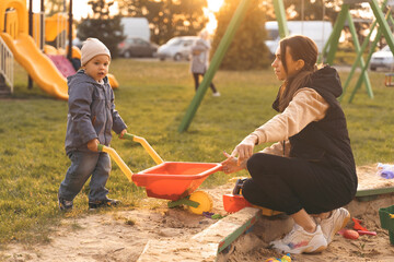 Mother and child playing with wheelbarrow in sandbox. Little builder. Education, and imagination, purposefulness concept. Support childhood parenthood symbol