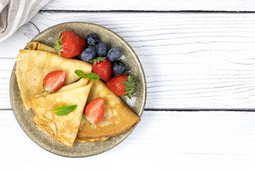 French crepes, pancakes or Russian bliny with berries on a white wooden background. Pancakes with berries. Russian pancakes. Pancakes week. Top view, copy space.