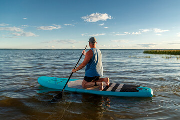 A man on his knees on a sup board in the evening at sunset.