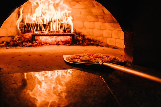 The chef puts the Margherita, four cheese or meat pizza on a shovel in the oven. A firewood oven for cooking and baking pizza. Italian traditional pizza is cooked in a stone wood-fired oven.
