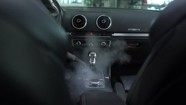 Steam cleaning of gearbox and dashboard in car 4k video. Vaping steam. Cleaning individual elements of black leather interior in auto. Creative advert for auto detailing service.