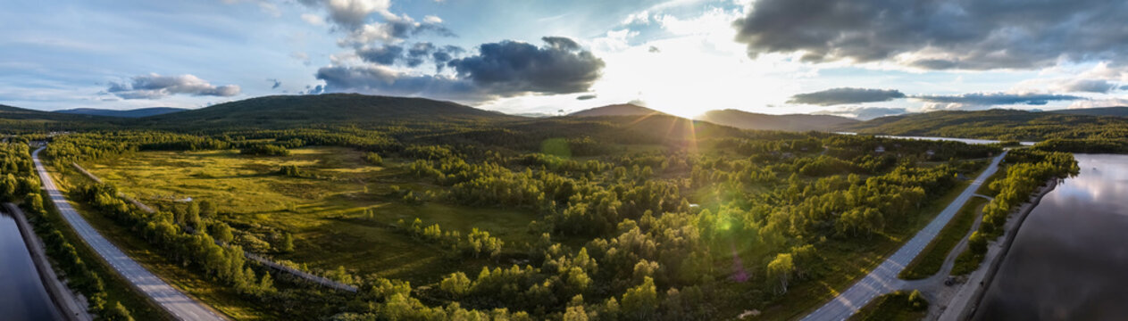 Scenic panoramic photo of sunset in Norway, camera lens flair. Summer evening