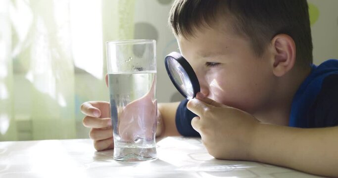 The child boy looking at water in a glass through magnifying glass