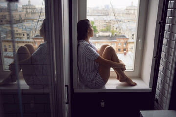 woman in striped pajamas sits on the windowsill in the bathroom in the morning and thinks about happiness.