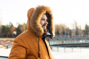 Outdoor winter portrait of handsome bearded man dressed in winter clothes, guy wears coat in snowy park - season and cold weather concept © satura_