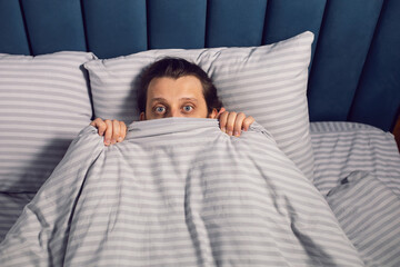 portrait of a man with a beard lying on the bed in the bedroom suffering from insomnia, lying with bulging eyes.