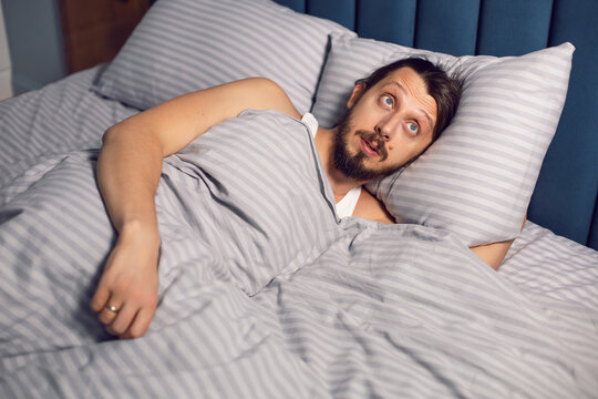 portrait of a man with a beard lying on the bed in the bedroom suffering from insomnia, lying with bulging eyes.